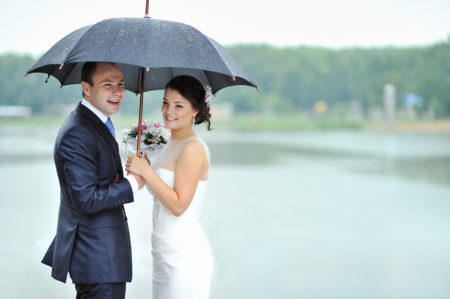Rainy wedding day. Bride and groom sharing black umbrella.