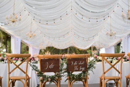 Head table with white linen and wooden chairs underneath white tent