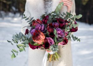 Winter bouquet with burgundy roses calla lilies and pink and purple flowers with greenery