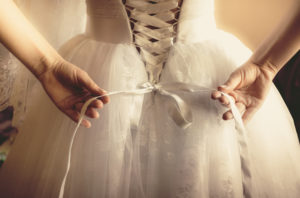 Closeup toned photo of beautiful bride tying up her wedding dress