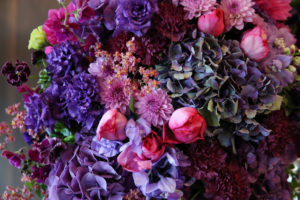 Round flower arrangement in silver stand with purple, pink, and magenta flowers, dahlia, rose, and hydrangea.